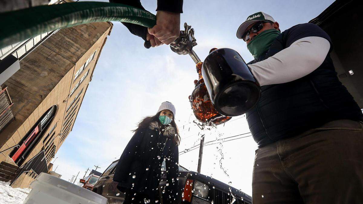 Macy Moore, co-owner of HopFusion Ale Works, left, fills up growlers with water for Aaron Villanueva, right, as Isabel Villanueva, 9, watches. North Fort Worth residents no longer need to boil water, but westsiders should continue until further notice.