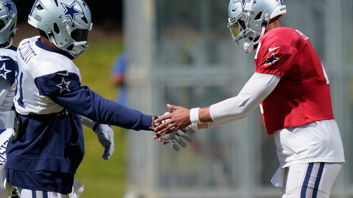 Dallas Cowboys quarterback Dak Prescott, right, and teammate running back Ezekiel Elliott (21) grab each others hands before participating in an NFL football team practice in Frisco on Thursday.