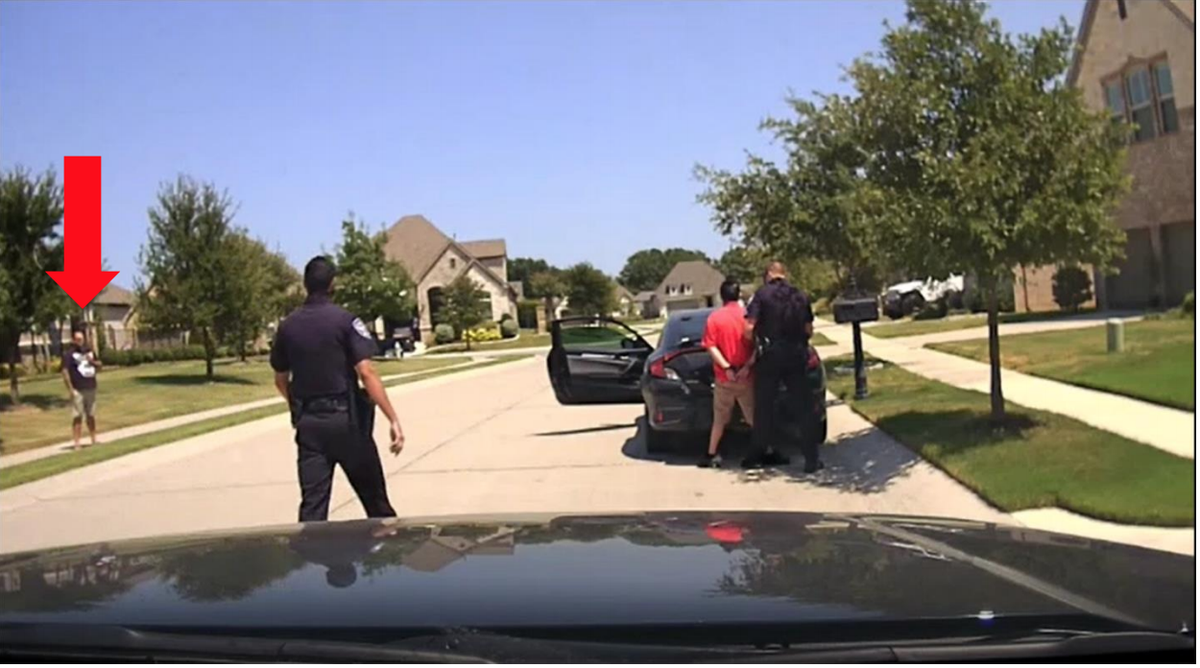 This photo shows the scene of Marco Puente’s arrest at the moment that Officer Antik Tomer arrived. The red arrow identifies Puente, who was standing on the sidewalk across the street filming on his cell phone