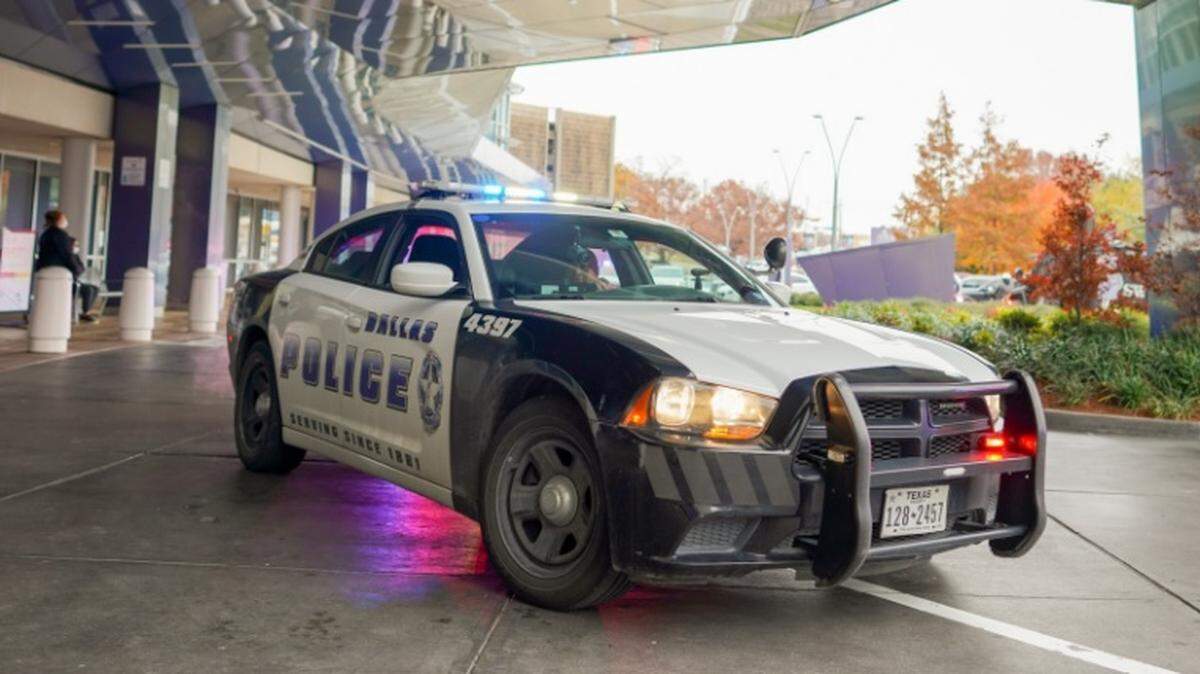 A Dallas police car sits under the overhang of a building. There are trees in the background.