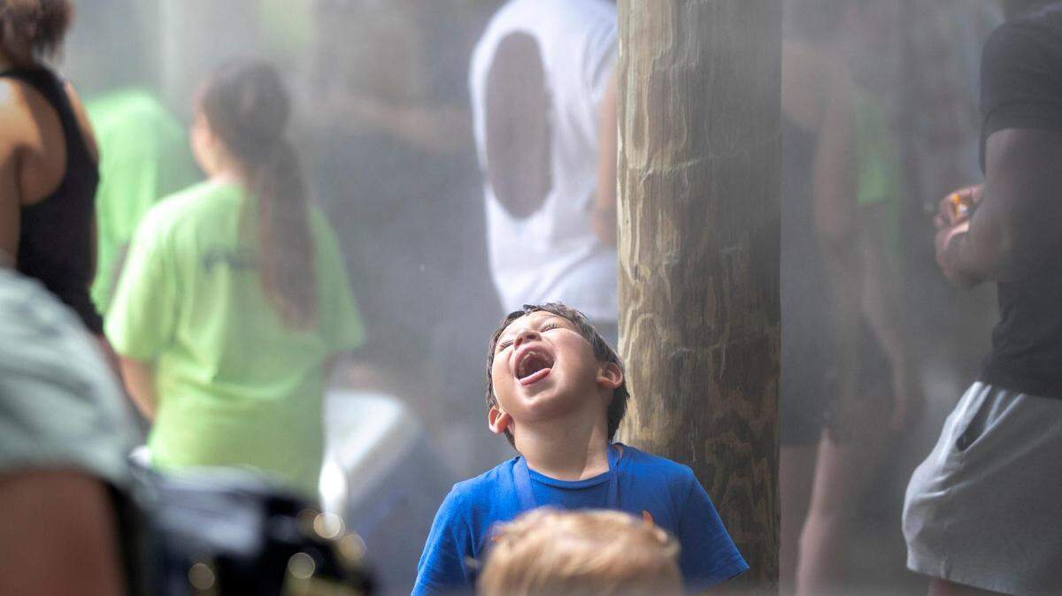 A boy lifts his head up with his mouth open as mist falls from above.