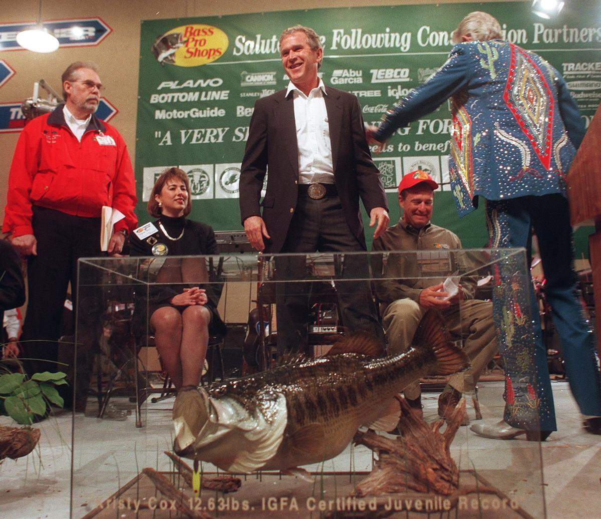 In this March 24, 1999, photo, then Texas Gov. George Bush laughs as he gets a pat on the back from country music legend Porter Wagoner before the opening remarks at the Bass Pro Shop Conservation Fundraiser. The other people on the stage are Grapevine Mayor William D. Tate, Vicki Truitt, and Bass Pro shop owner John l. Morris. 