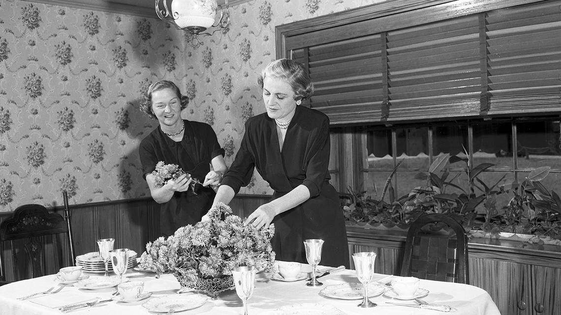 Nov. 1, 1952: Society series on Thanksgiving table settings. Finishing Touches: At the home of Mrs. W.O. Kelly, 1825 Oakland, she is assisted by Mrs. Jack Kelly in putting the last posies in place before the family dines. Damask, imported china and silver set this table.
