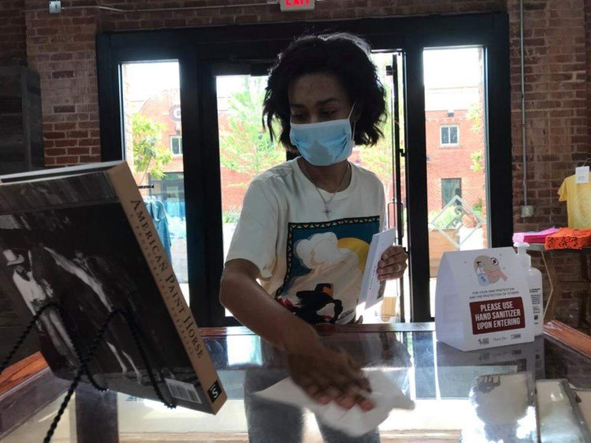 Terie Lei Moore wipes down a counter-top inside PH Barn Door in the Fort Worth Stockyards on Saturday morning. She was disinfecting high-touch surfaces every hour as the business welcomed customers into the store, though it could only be at 25 percent capacity.