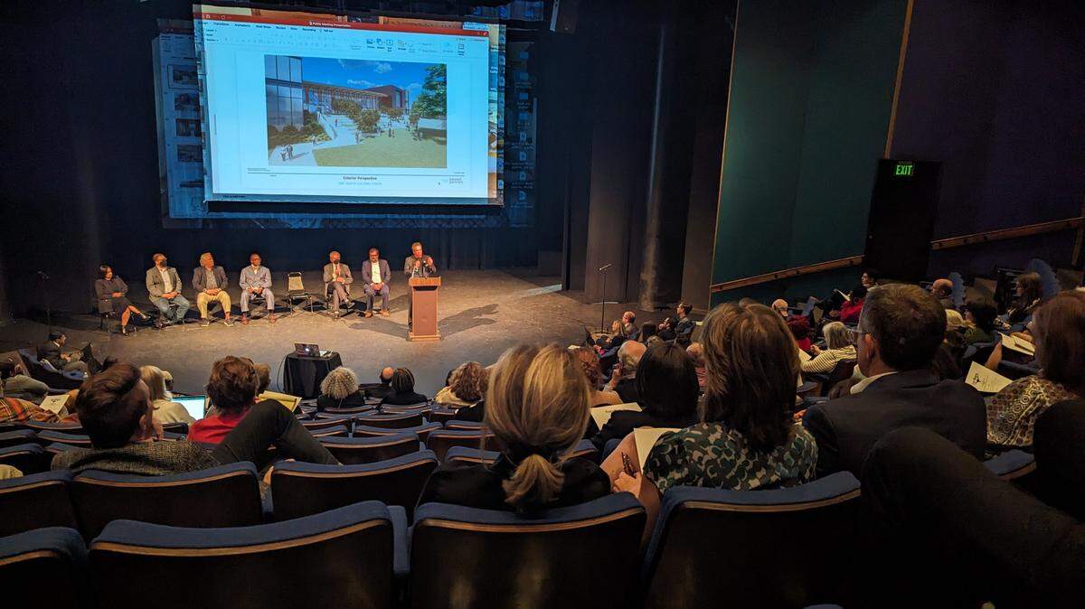 A stadium seating theater with people watching a power point presentation on stage. 