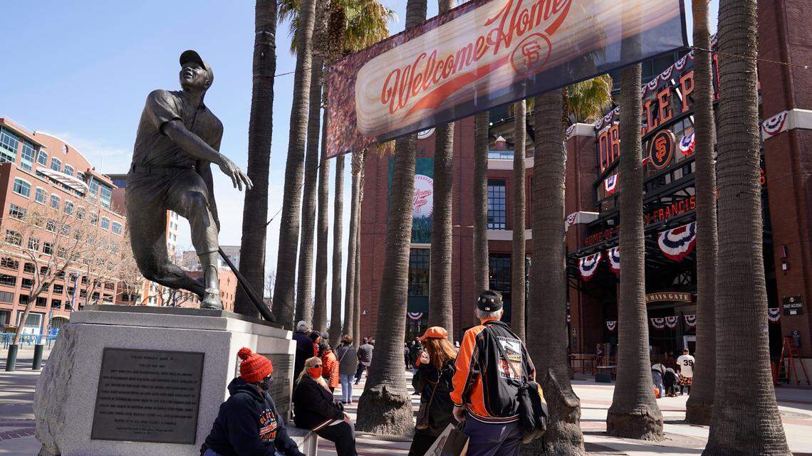 People wait by the statue of baseball great Willie Mays for the gates at Oracle Park to open before the start of an opening day baseball game between the San Francisco Giants and the Colorado Rockies, Friday, April 9, 2021, in San Francisco. (AP Photo/Eric Risberg)