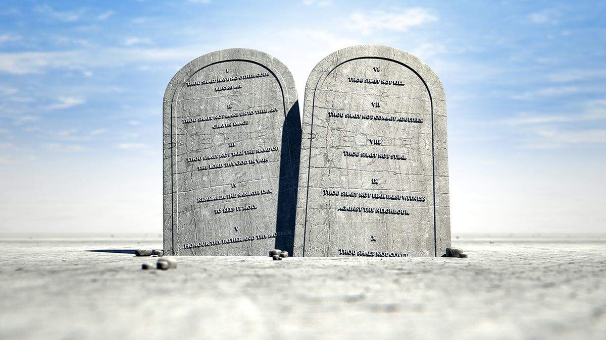 Two stone tablets with the ten commandments inscribed on them standing in brown desert sand in front of a blue sky