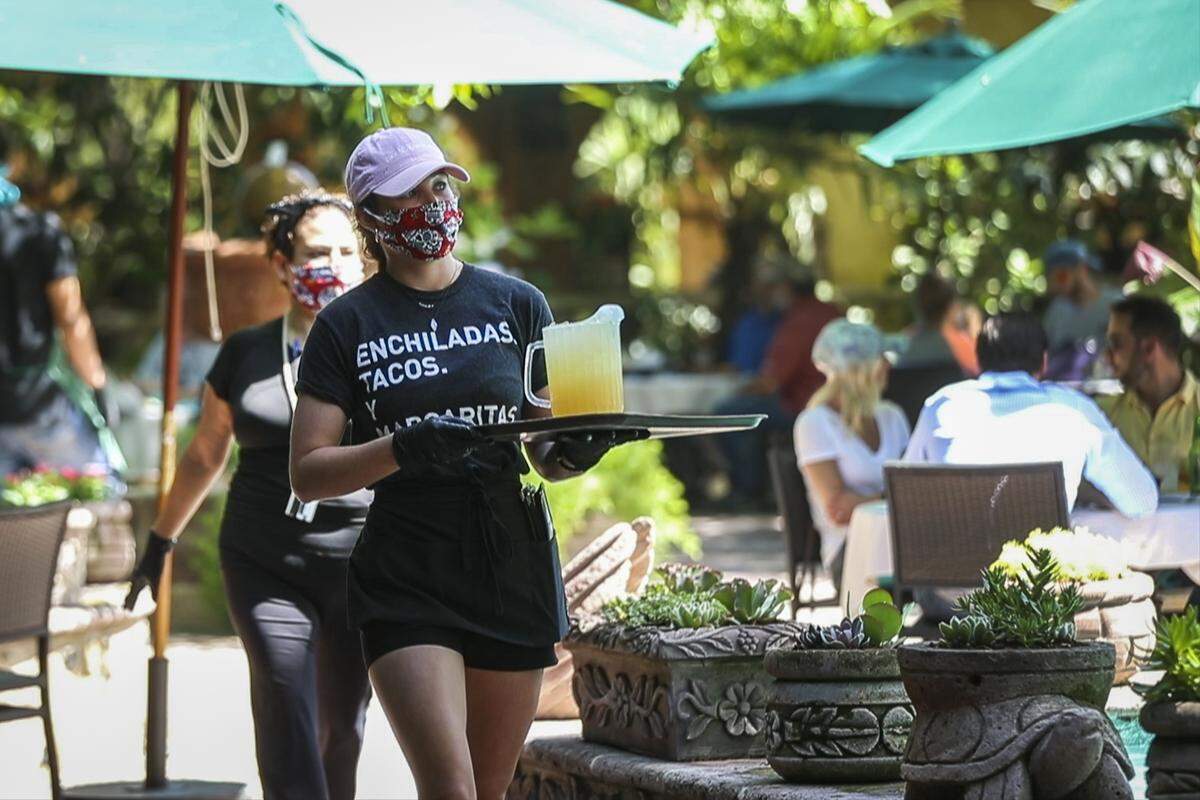 A waitress wears mask and gloves while serving lunch at Joe T. Garcia’s amid the coronavirus outbreak Friday, May 1, 2020, in Fort Worth.