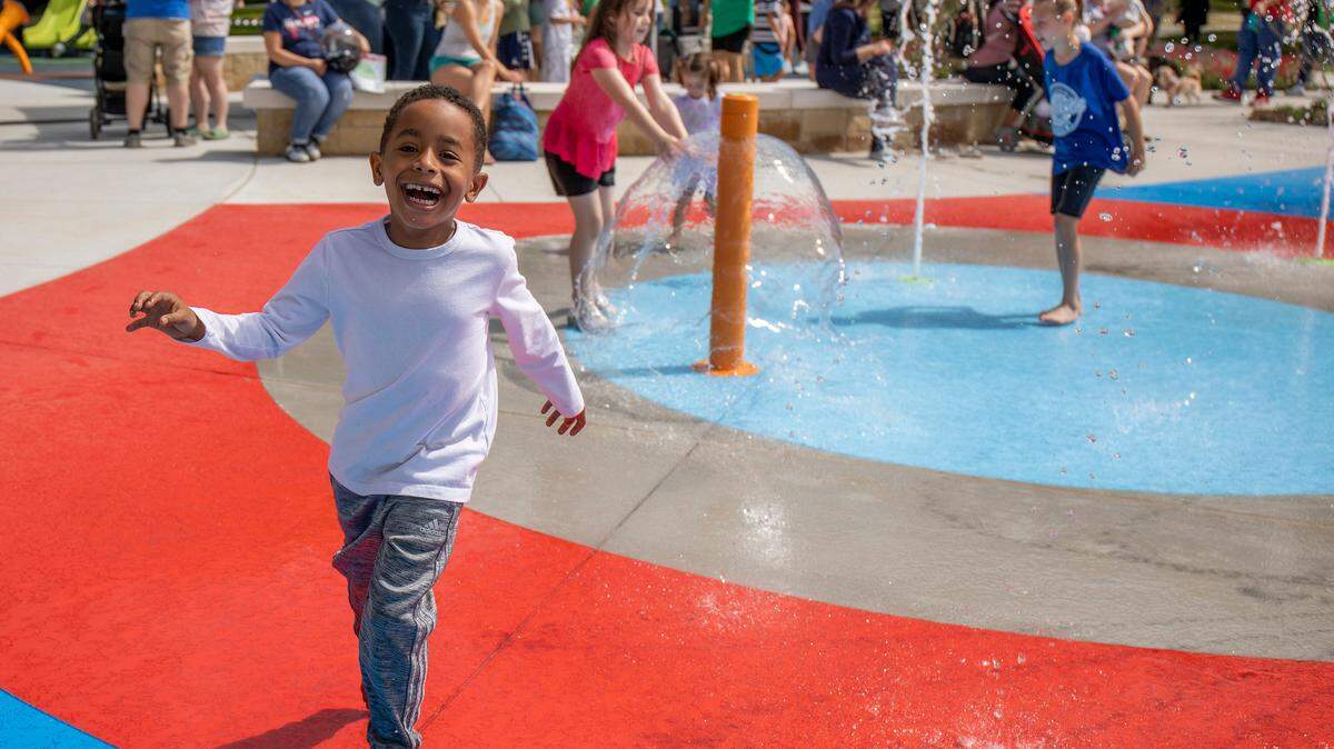 Children run around the edges of a splash pad.