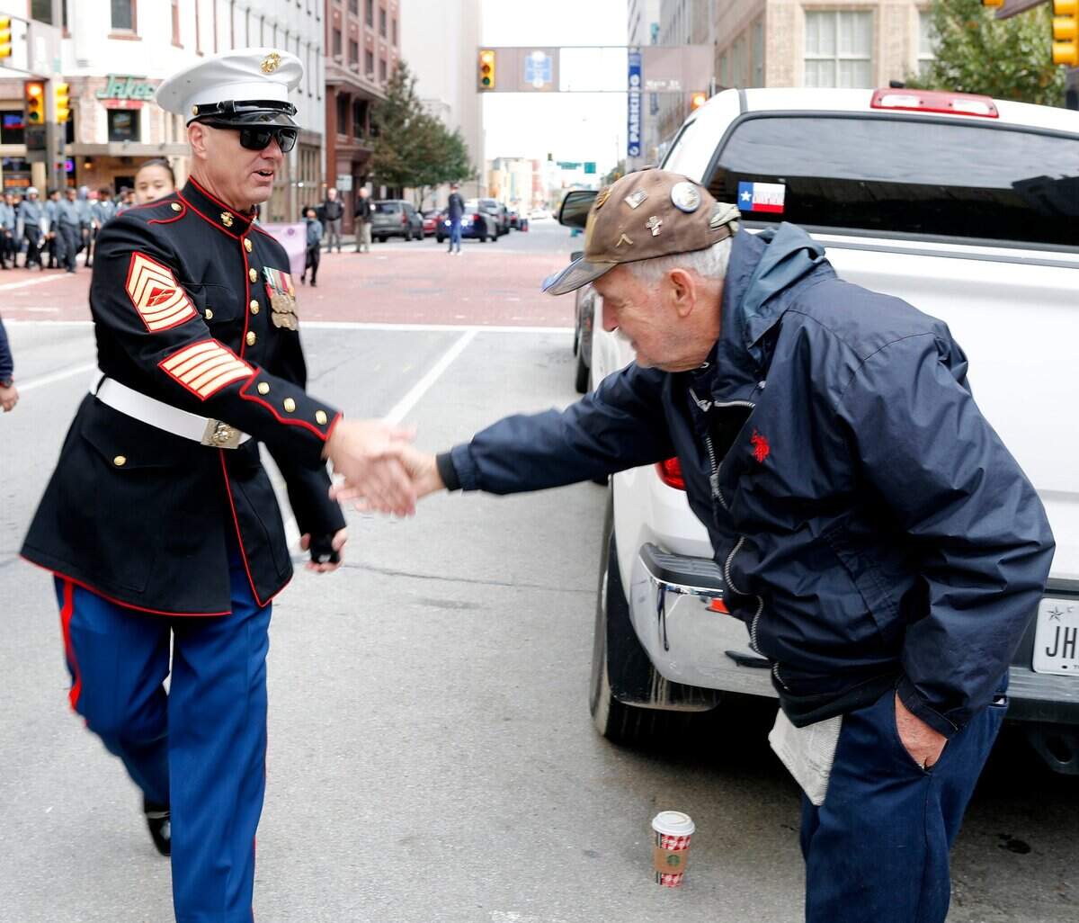 Nov. 10, 2018: Former Army Pfc. Ken Noveroske shakes the hand of Marine Master Sgt. Grames during the Tarrant County Veterans Day parade in Fort Worth. Noveroske, who served in Germany, posted up at a corner and shook hands with as many uniformed service members as he could. JROTC students from several local schools participated in the parade honoring veterans.