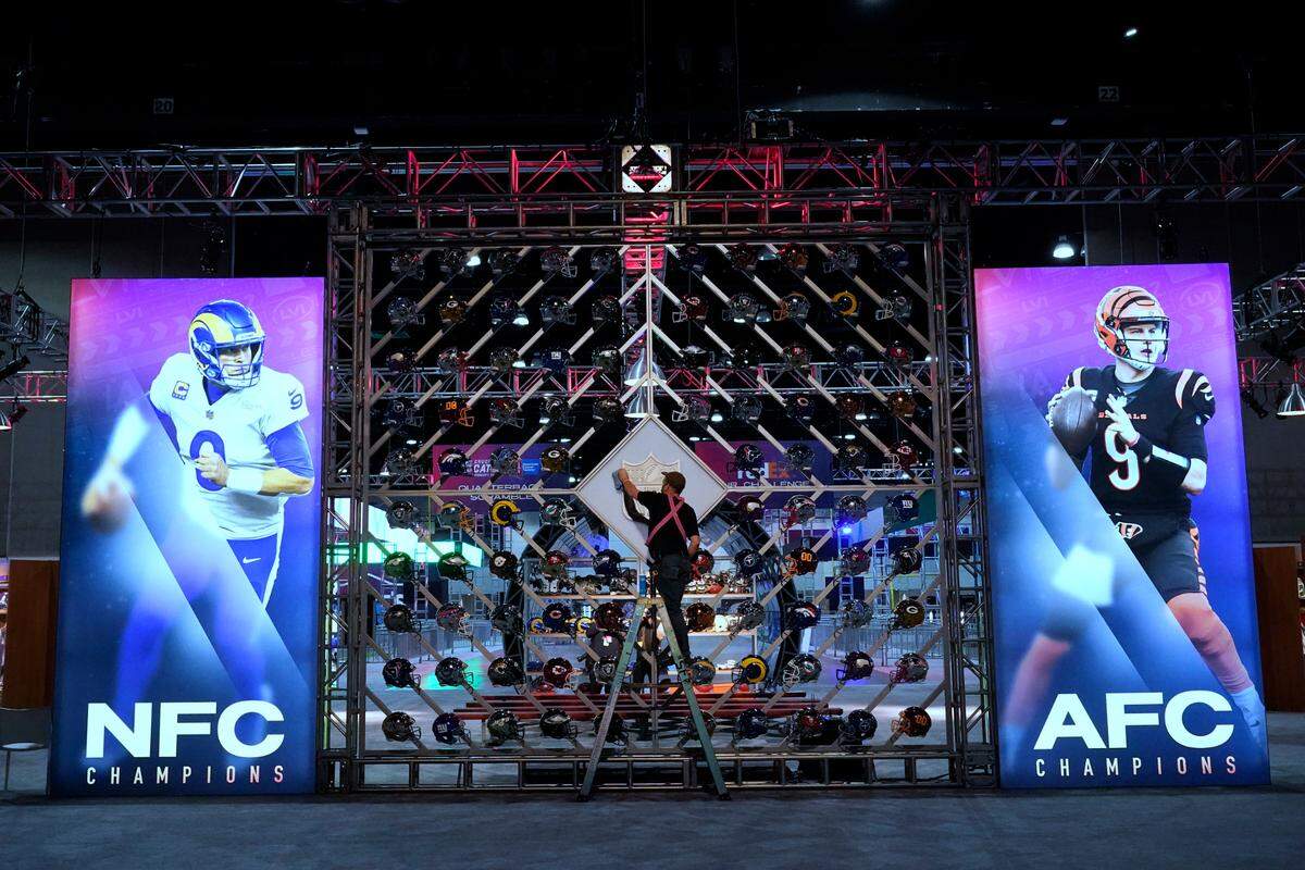 A worker cleans a league logo between images of Los Angeles Rams quarterback Matthew Stafford, left, and Cincinnati Bengals quarterback Joe Burrow inside the NFL Experience, an interactive fan show, Friday, Feb. 4, 2022, at the Los Angeles Convention Center in Los Angeles. The Los Angeles Rams play the Cincinnati Bengals in the Super Bowl NFL football game on Sunday, Feb. 13. in Inglewood, Calif. (AP Photo/Marcio Jose Sanchez)