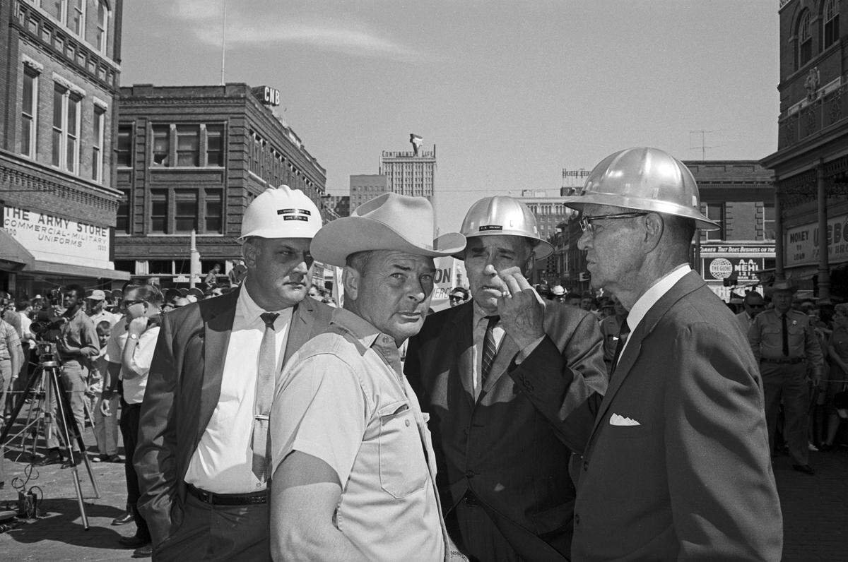 Ray Hollis, the owner of West Texas Demolition Co. stares down a photographer just before demoltion began, as county officials huddle behind him. From left are: J. Ernest Fender Jr. of Acme Brick, Ray Hollis of West Texas Demolition, County Commissioner Clarence H. “Punch” Wright and County Auditor J. M. “Star” Williams.