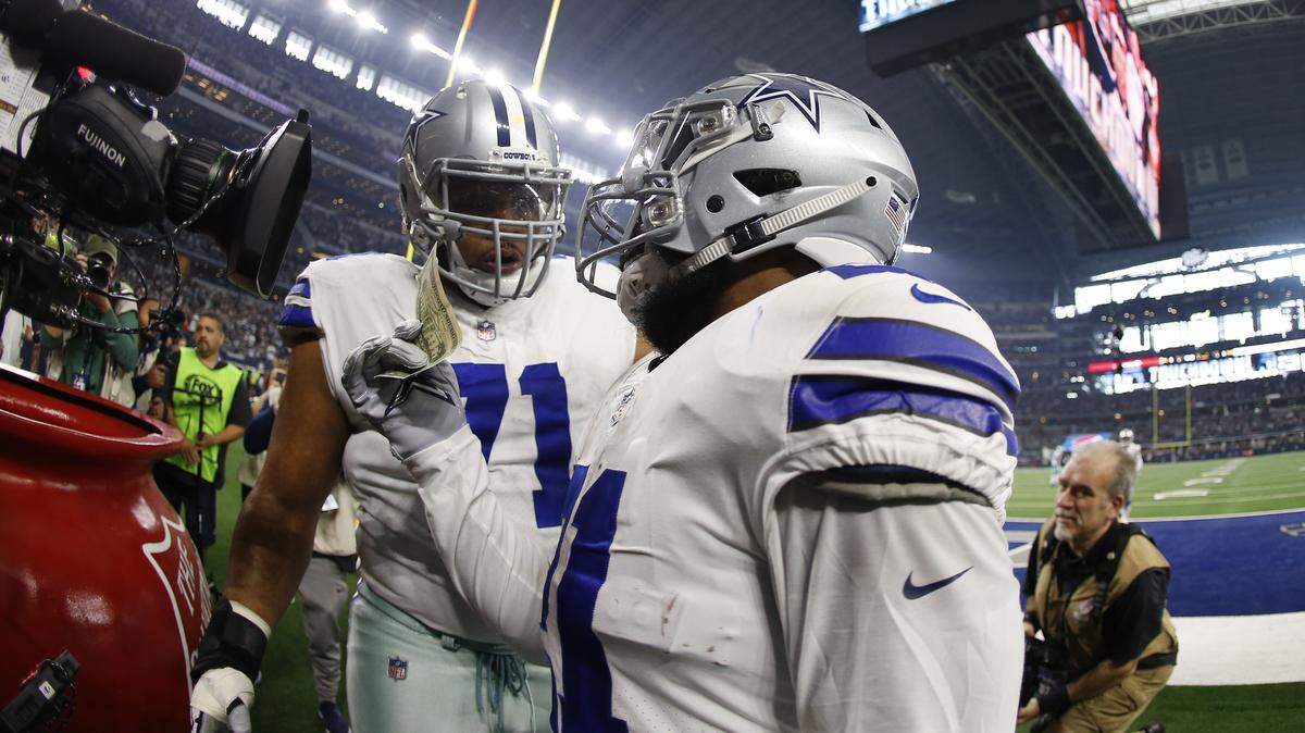 Dallas Cowboys running back Ezekiel Elliott (21) pulls out a twenty dollar bill to put in the Salvation Army kettle after scoring a touchdown against the Washington Redskins during the first half of an NFL football game in Arlington, Texas, Thursday, Nov. 22, 2018. (AP Photo/Ron Jenkins)