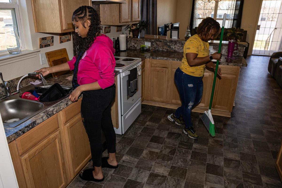 Smith’s youngest daughter, La’Nisha Campbell, left, washes dishes while her she sweeps the floor in the kitchen of their new home. Smith and her two daughters have moved between apartments over the past decade.