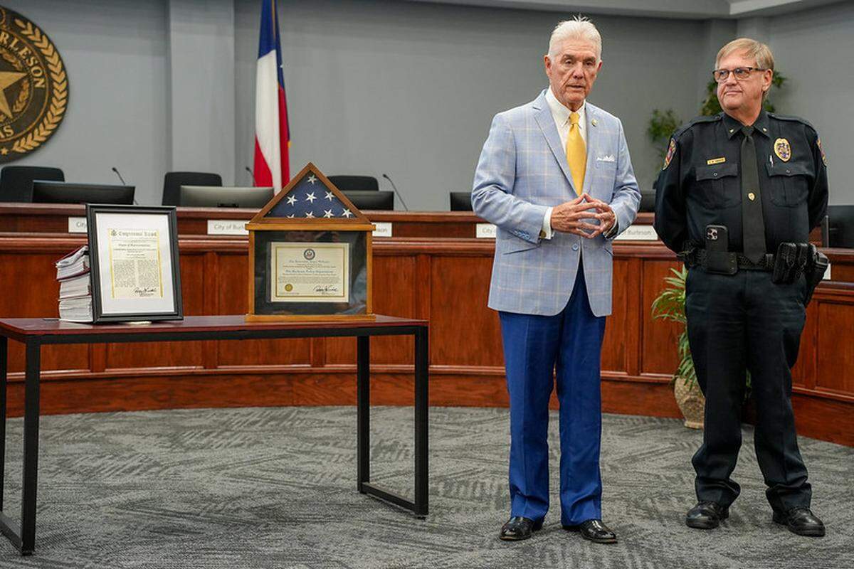 U.S. Rep. Roger Williams (left), representing Texas’ 25th congressional district, presents a framed copy of the Congressional Record and a flag that had flown over the U.S. Capitol to Burleson Deputy Chief of Police Doug Sandifer at a ceremony at Burleson city hall on Aug. 15, 2025. Williams was in Burleson to honor the police department for its Victim Assistance Poster Program.