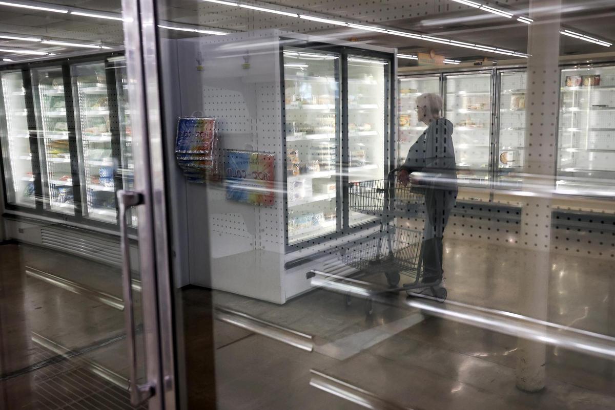 A shopper is reflected in empty freezer cases at Burleson’s independent grocery store City Market on Wednesday, Feb. 5, 2025.
