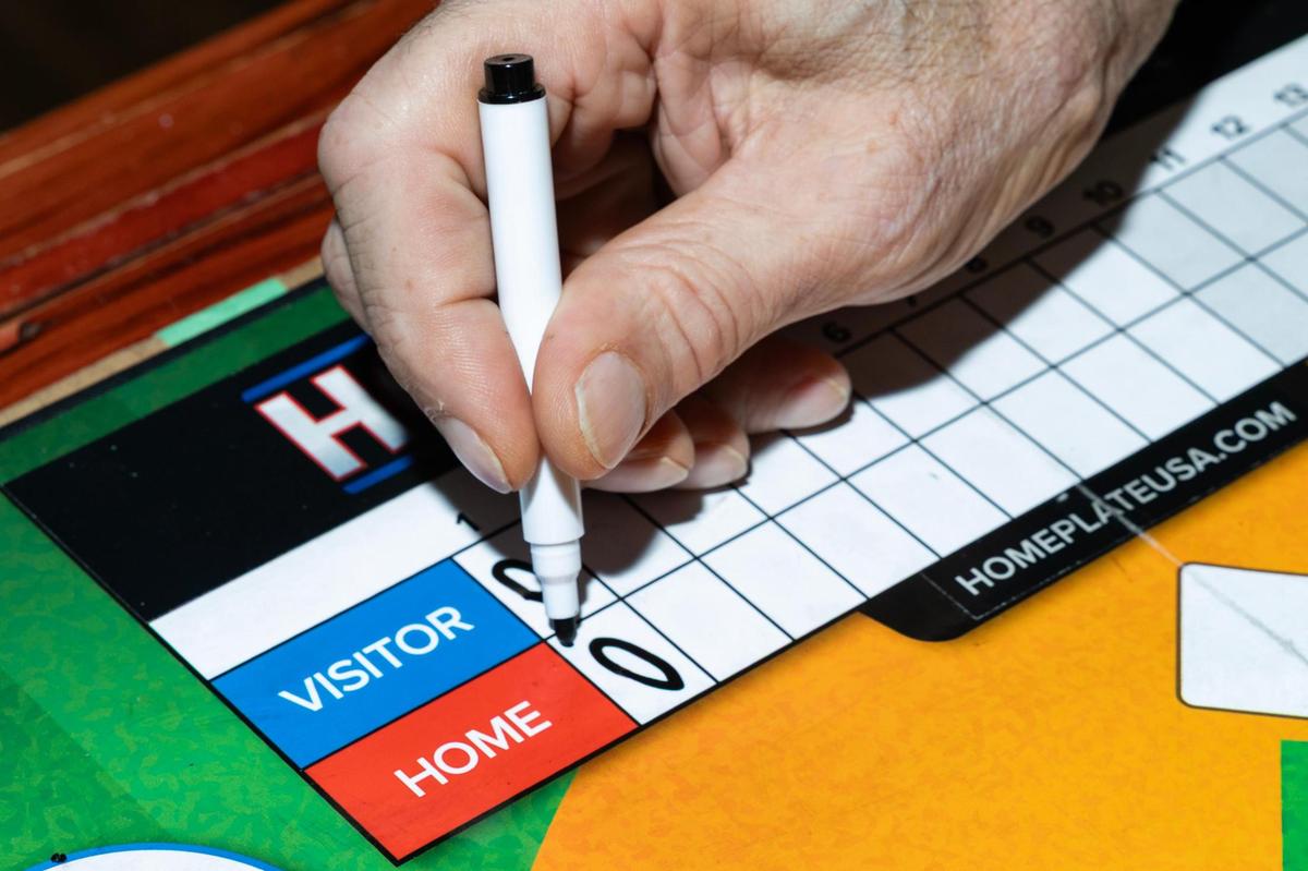 Miguel Otero, the creator of Homeplate USA, shows how the game is played in his apartment in Grapevine on Wednesday, April 16, 2025. Otero invented Homeplate USA, a baseball board game, when he was 11. Now retired at 67, he began producing and selling the game in March out of his apartment.