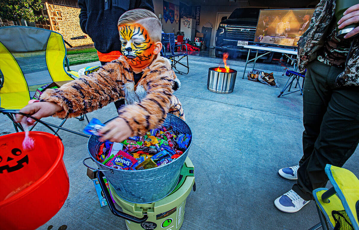 Slade Middlebrook, 4, passed out treats on his driveway in the Main Place subdivision in Acton on a chilly Halloween night Tuesday, Oct. 31, 2023. A propane fire pit sat on the concrete driveway and a big screen television had the World Series game 4 that the Texas Rangers won 11-7.