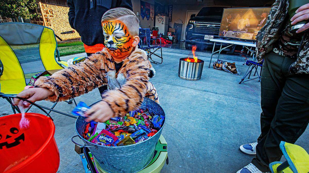 Slade Middlebrook, 4, passed out treats on his driveway in the Main Place subdivision in Acton on a chilly Halloween night Tuesday, Oct. 31, 2023. A propane fire pit sat on the concrete driveway and a big screen television had the World Series game 4 that the Texas Rangers won 11-7.