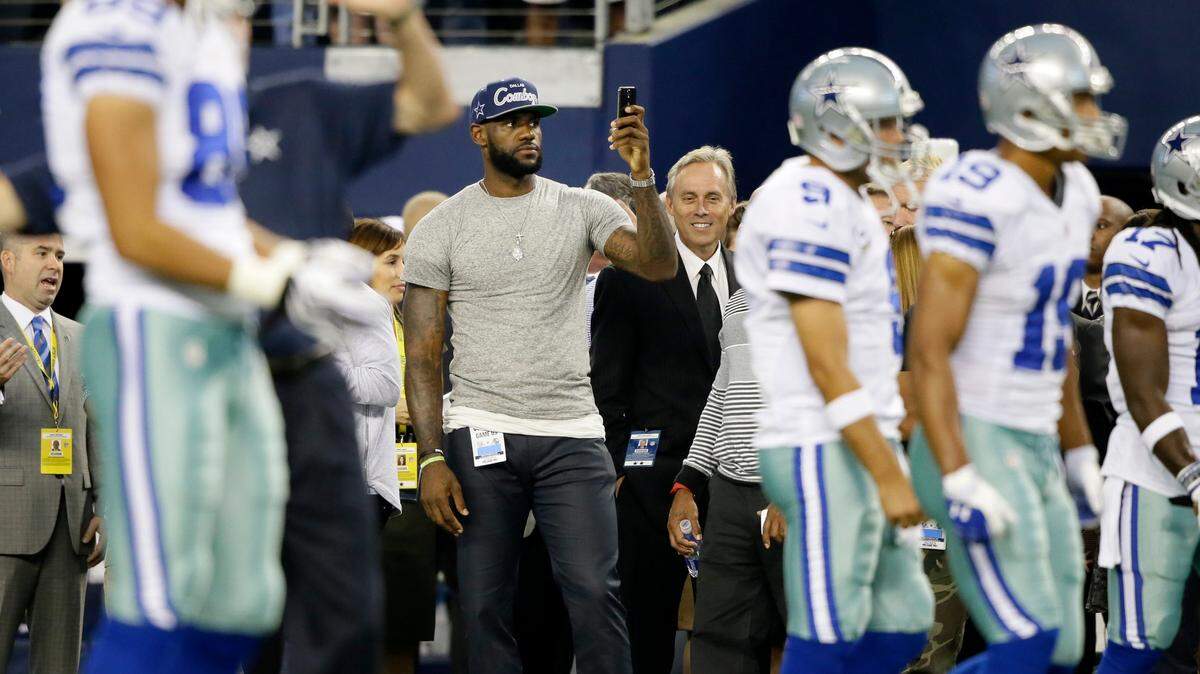 NBA basketball player LeBron James, center, takes pictures on the field before an NFL football game between the Dallas Cowboys and the New York Giants, Sunday, Sept. 8, 2013, in Arlington.