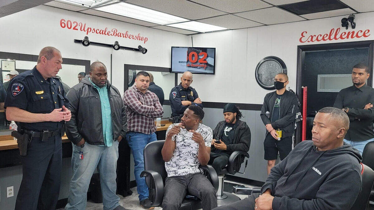 Two customers sit in barbershop chairs while two police officers stand around them. 