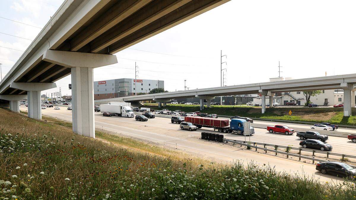 Traffic flowing on a highway, left to right, can be seen in the distance framed by a grassy embankment on the bottow left and an elevated ramp on upper left.
