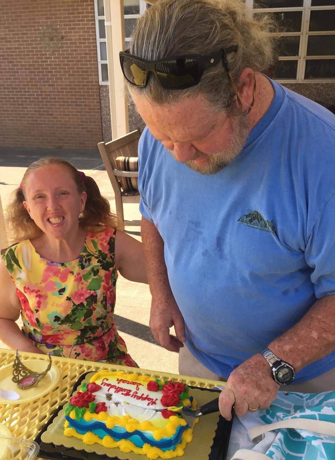 Sarah Danks (left) smiles as her father, Mike Danks (right), cuts into her birthday cake. Mike and his wife, Karen Danks, have been able to communicate with Sarah over the phone as she has been isolated in her apartment at the the Denton State Supported Living Center, where there have been 45 coronavirus cases.