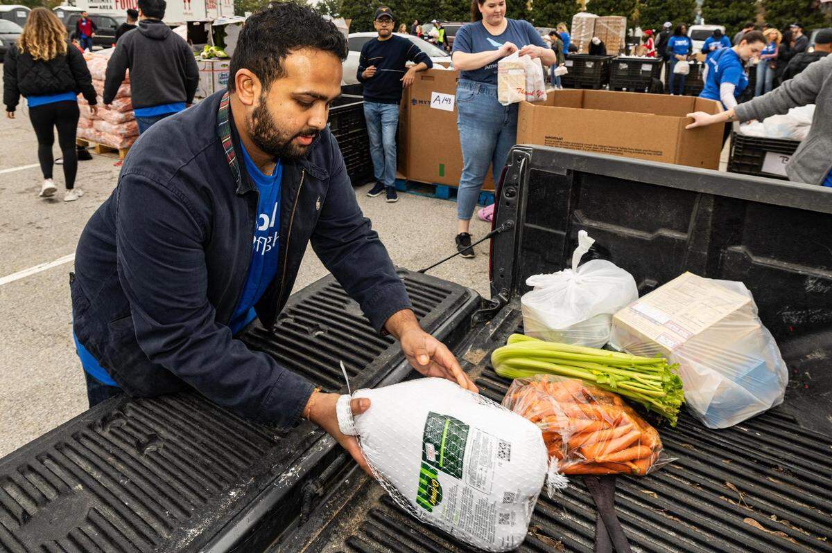 Shashank Menon puts various Thanksgiving-related groceries into the trunk of a car during the 4th annual Thanksgiving Mobile food distribution at AT&T Stadium in Arlington on Friday, November 17, 2023.