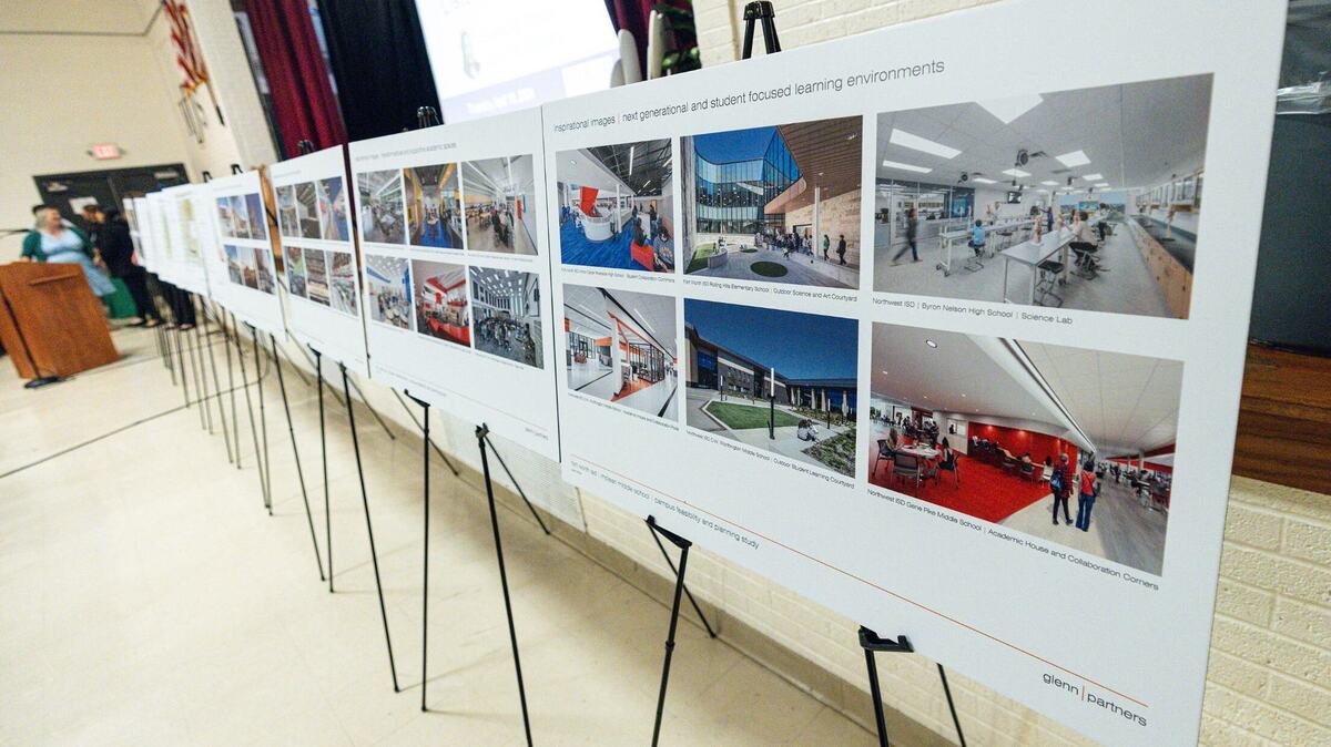 Computer-generated images of school buildings hang on easels in a school auditorium.