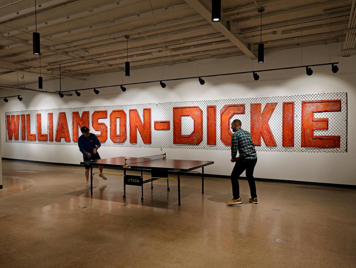 Dickies associates take a small work break in front of the original Williamson-Dickie sign at Dickies offices in downtown Fort Worth Texas, Thursday Mar. 28, 2024. The 102 year old work apparel company recently relocated to downtown Fort Worth. (Special to the Star-Telegram Bob Booth)