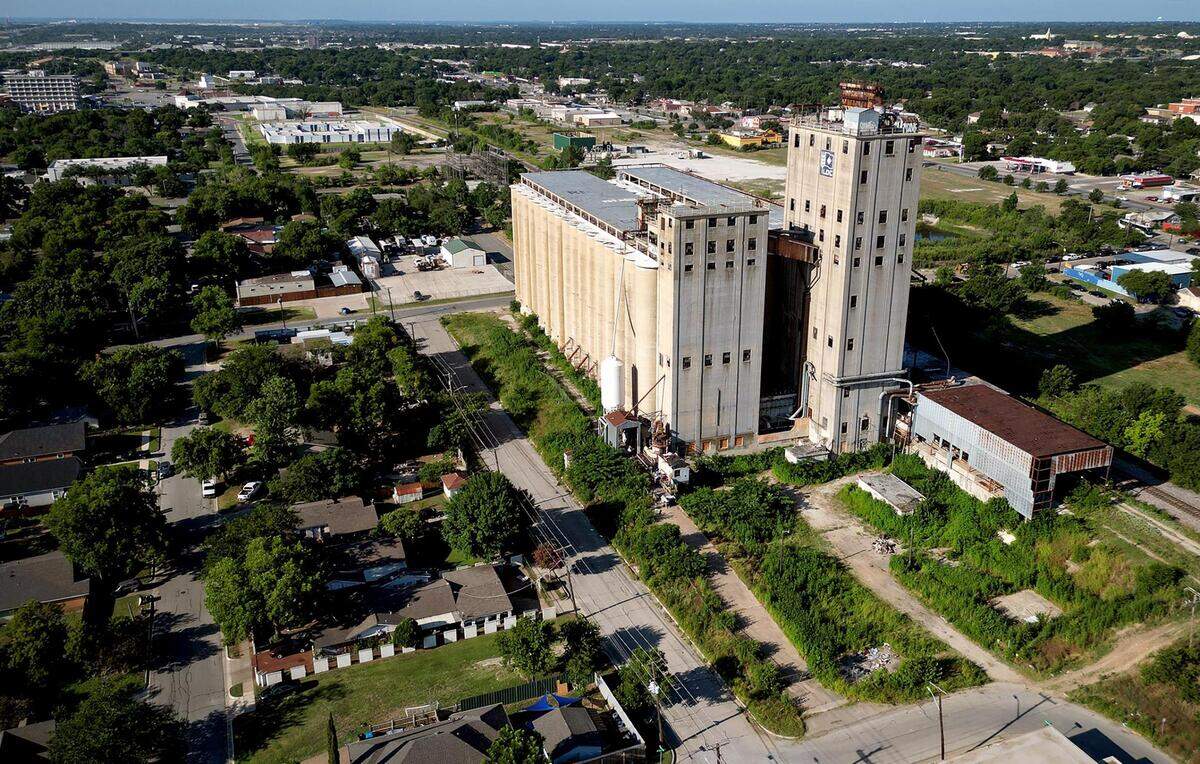 A drone photo of a very tall large building surrounded by one story homes and trees.