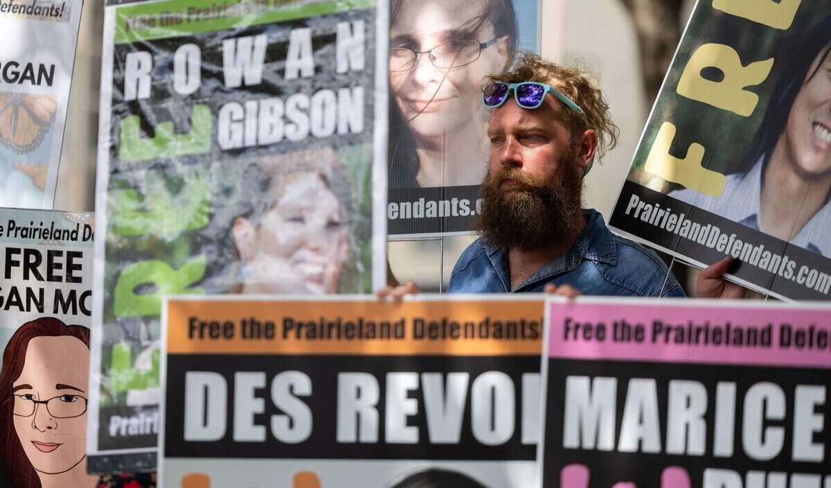 Surrounded by signs, Kolin Kilpatrick listens to a speaker talk in support of the defendants during the sentencings of the Prairieland Ice Detention Center terrorism case on Wednesday, July 1, 2026, in Fort Worth, Texas. Supporters opposing the sentencings held a press conference in front of the Federal Courthouse in which family members and friends of the defendants spoke.