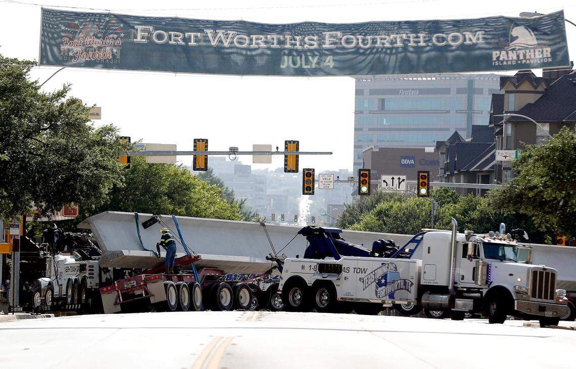 Tow trucks try to stabilize a concrete support beam carried by a truck that became stuck at the intersection of Henderson and West 7th Streets on Friday, June 21, 2019.