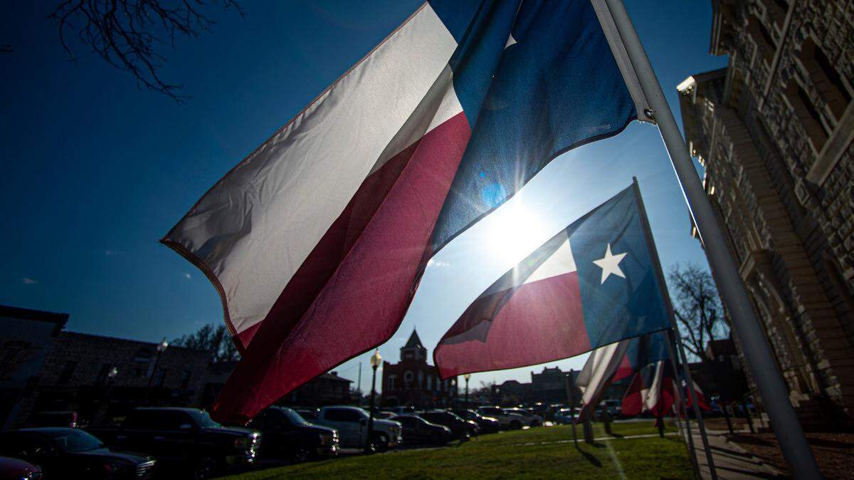 A late afternoon sun lights up Texas flags at the old Hood County Courthouse on the Historic Granbury Square on March 19, 2021.