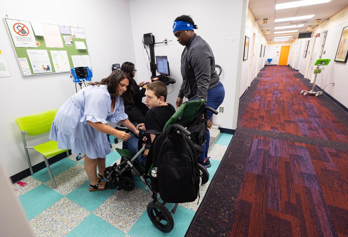 Meghan Czarobski, left, and licensed vocational nurse Lakeisha Tilmon, right, assist Preston Benjaman-Sewell out of his stroller to be weighed during an appointment at Cook Children’s Dodson Specialty Clinics in June.