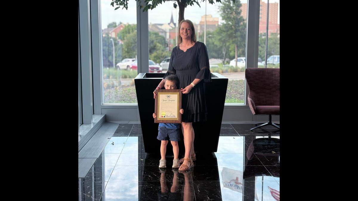 Kendra Frank stands alongside her 4-year-old son, Elliott, holding the special recognition plaque for Apraxia Awareness Day.
