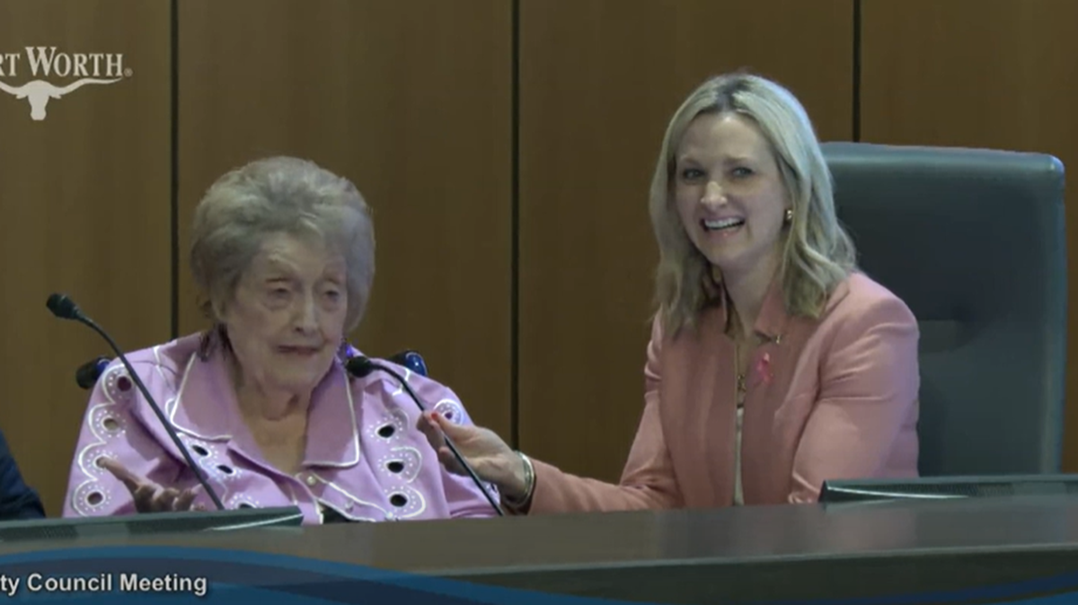 An old lady on the left sitting next to a young blond lady behind a city council dais.