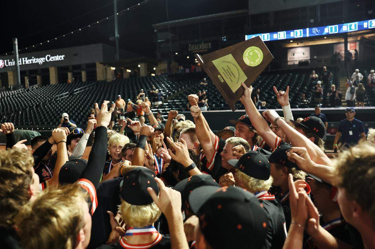 Aledo players break out of a huddle while a player holds up the championship trophy after the Class 5A Division I playoffs state championship game at Dell Diamond Stadium on Friday, June 6, 2025.
