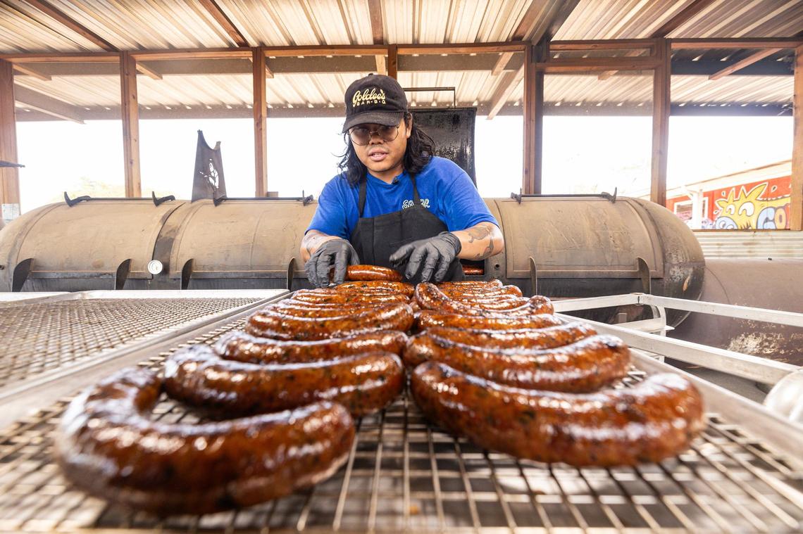 Nupohn Inthanousay, a co-owner of Goldee’s Barbecue, takes the smoked Lao sausage out of the smoker and onto cooling racks at Goldee’s prior to service in Fort Worth on Friday, June 28, 2024.
