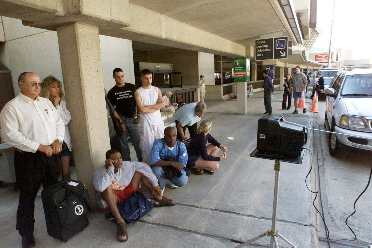 Stranded passengers outside DFW International Airport’s Terminal C, watch a television set up by a news crew to keep up with developments after a terrorist attack on the United States.