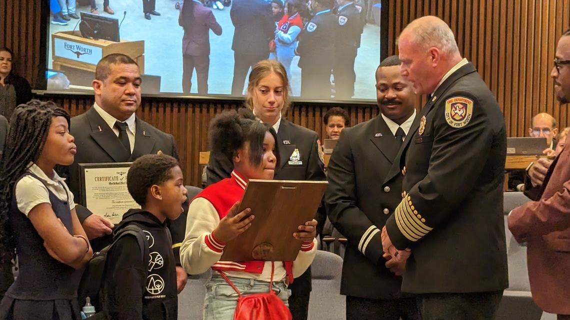 A girl holds a plaque surrounded by adults and her siblings in a city council chamber. 