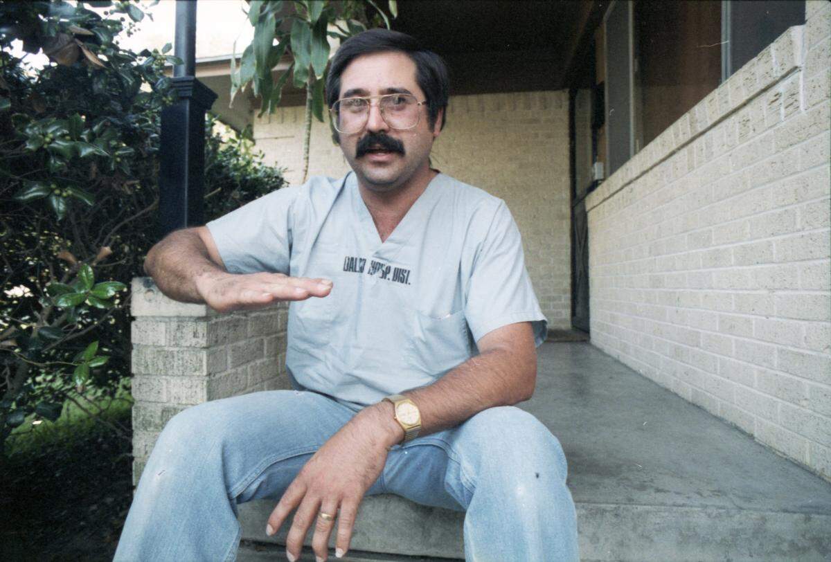 A man sits on outdoor steps making the motion “chest high” with his right hand.