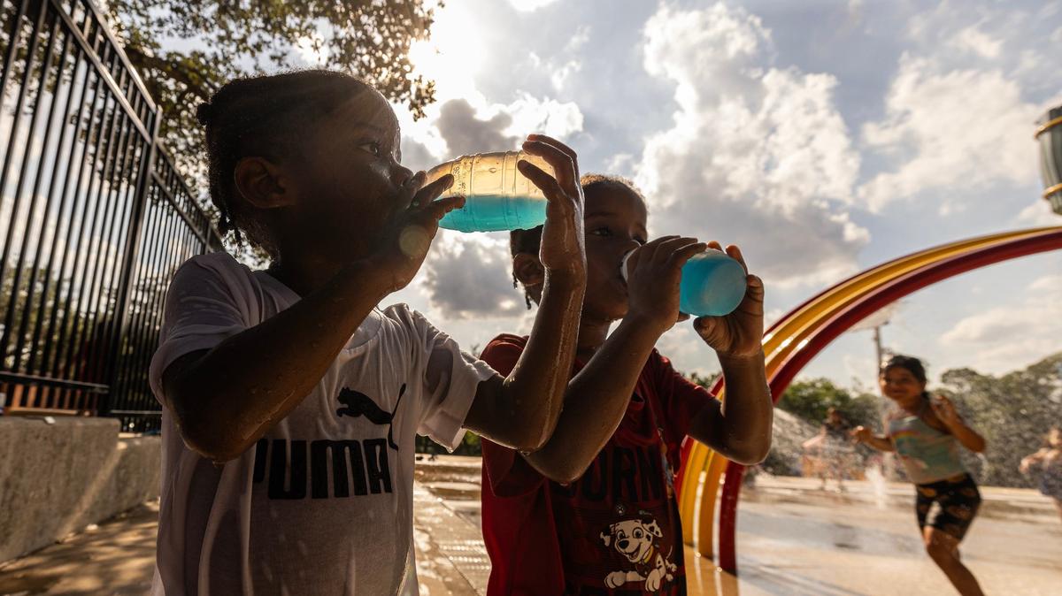 Twin brothers Enoch and Sampson Lee, 4, drink refreshments in the triple-digit heat at the splash pad at Sycamore Water Park in Fort Worth on Thursday, June 27, 2024.Temperatures rose to over 100 degrees as the summer heatwave begins to heat up.