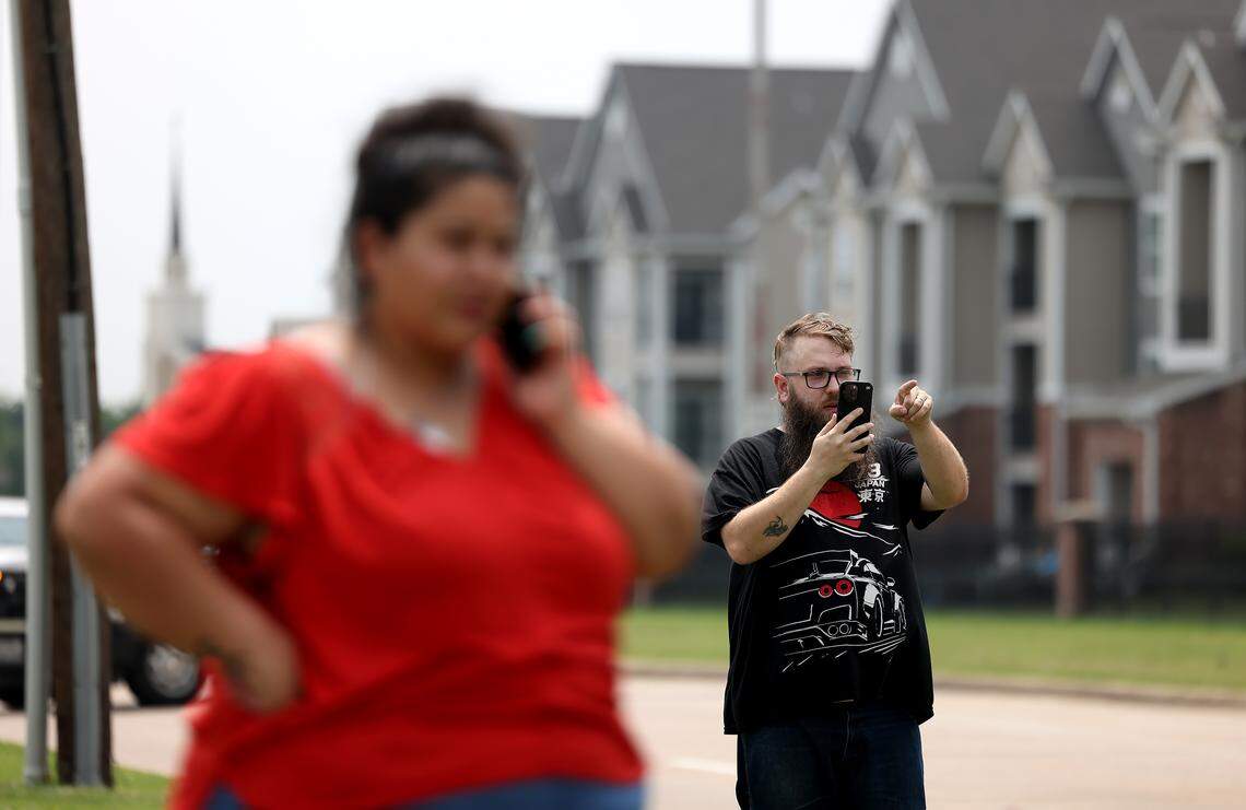 Fort Worth resident Eric Nerren, right, watches as a massive police presence works the area near the intersection of Basswood Boulevard and North Riverside Drive on Tuesday, April 28, 2026. Nerren, who lives in an apartment complex nearby, said he rushed home to check on his family when he received notification of an active shooter.