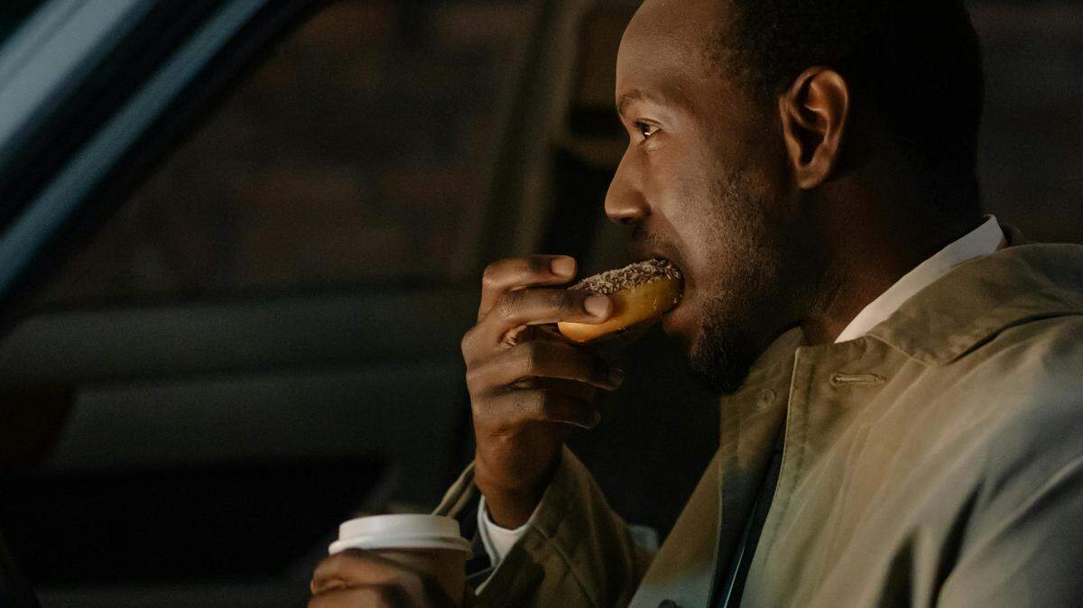 A man eating a donut and holding a cup of coffee in a car. Used with the Creative Commons license.