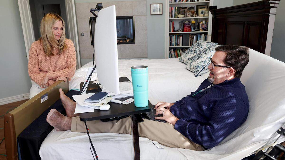 Karl Travis, right, sends an email while talking to his wife, Jaci, from the hospital bed set up for his in-home hospice care.