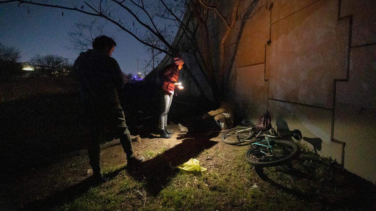 Two people talking to a homeless person at night. 