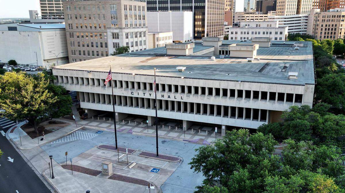 An aerial view of a three story building with City Hall in letters on the front. City buildings can be seen in the background. 