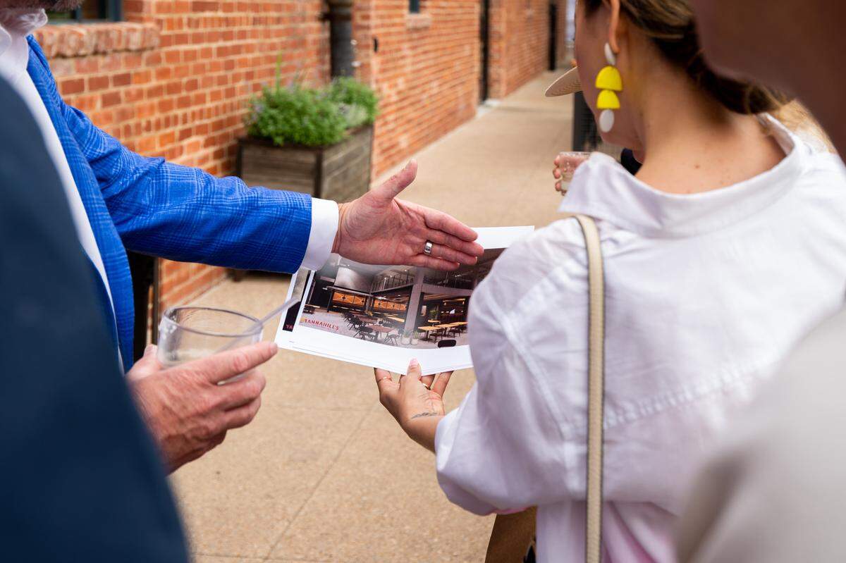 A man left of frame points to a piece of paper held by a woman right of frame that has a rendering of the finished Tannahill’s Tavern & Music Hall.