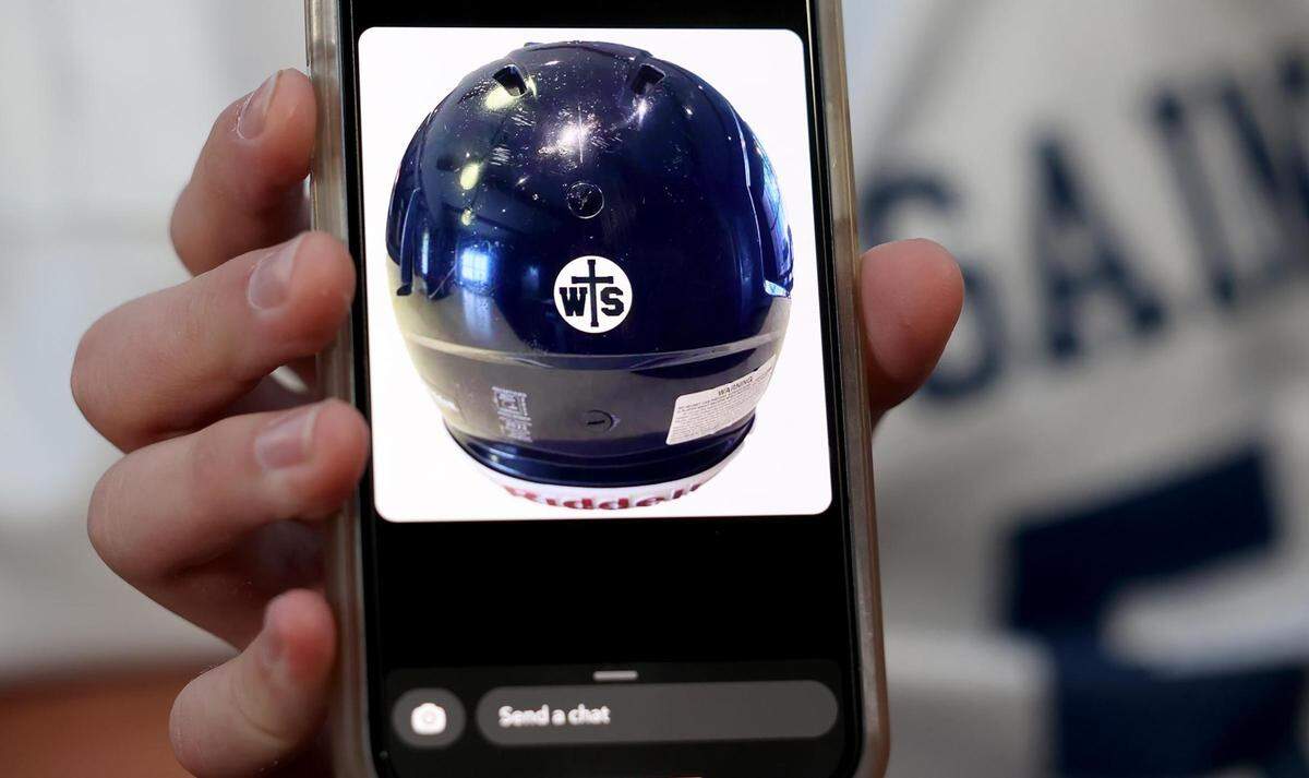 Oliver Bennett, 14, shows a photo of a sticker that the All Saints’ Episcopal Middle School’s football team placed on their helmets in memory of their coach, Wes Smith, on Wednesday, September 6, 2023, in Fort Worth. Smith was shot and killed in an apparently random act of violence on Friday.